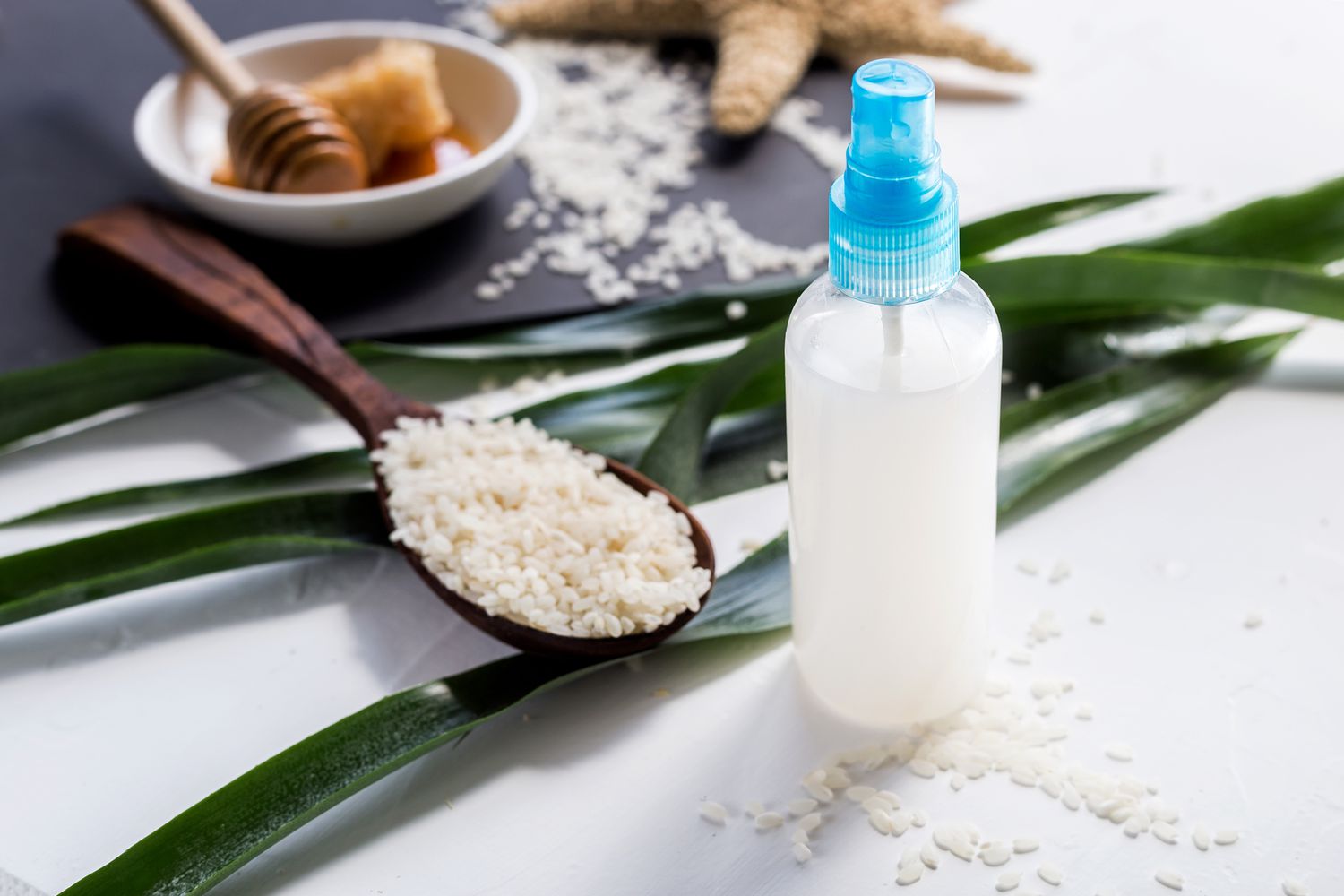 Spray bottle of rice water surrounded by rice and honey