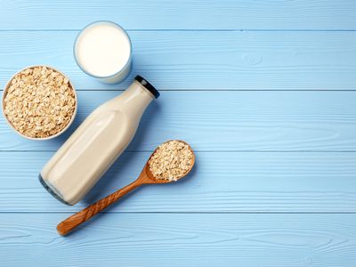 Glass of oat milk with raw oats on blue background