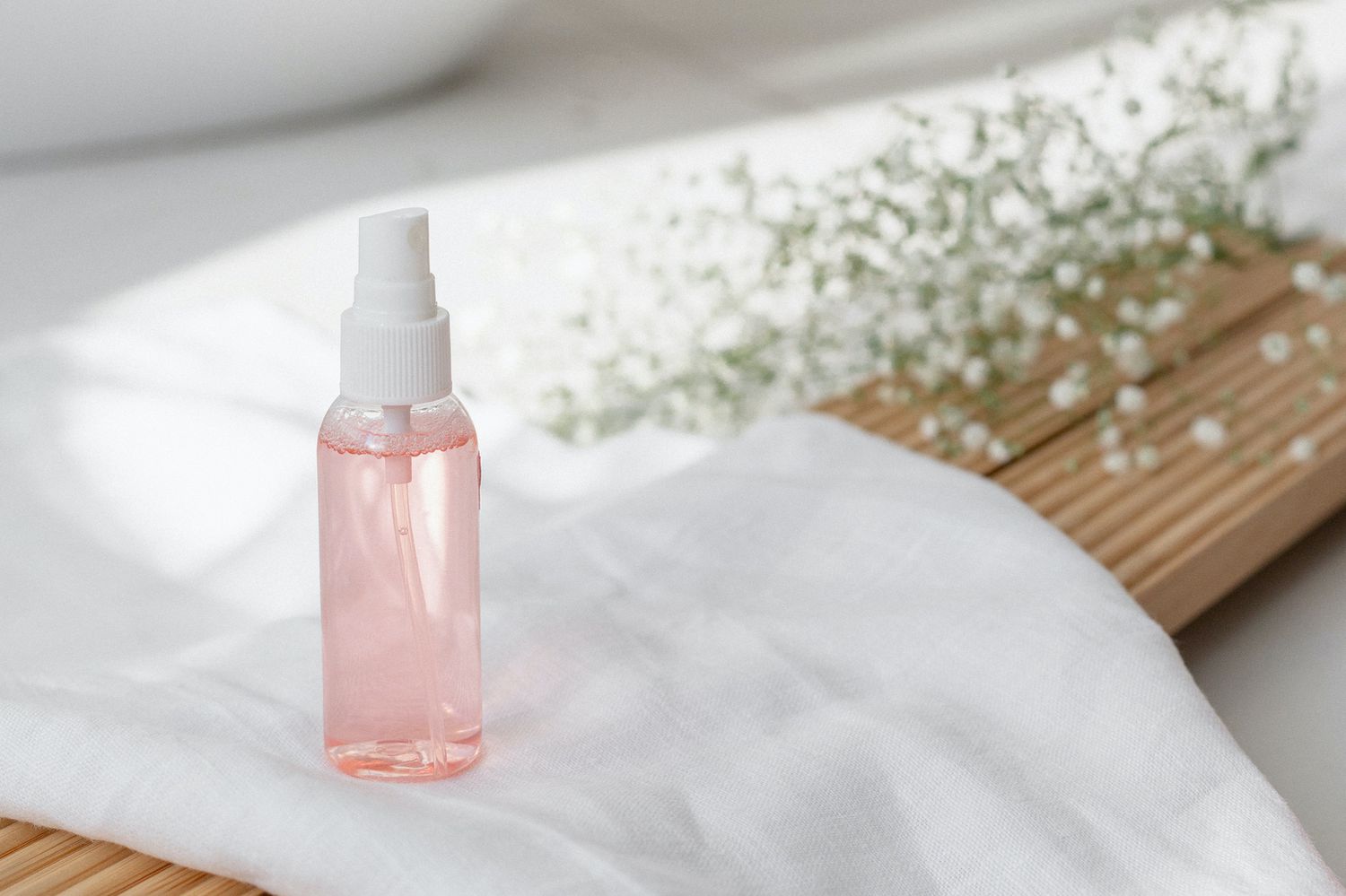 Spray bottle of rose water with Gypsophila flowers in background