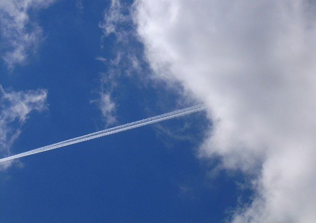 A contrail streaks out of some clouds
