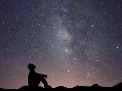 Silhouette of a person sitting on the ground looking up at star filled sky