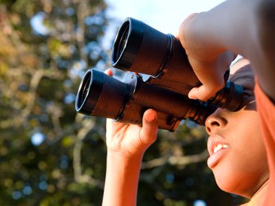 A boy looking through binoculars standing under a tree