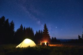 campers under a starry night sky with illuminated tent behind them