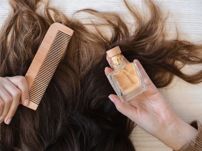 woman's long hair is spread out on floor while she holds comb and castor oil