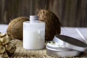 Coconuts and coconut oil in a metal pot. Wooden background.
