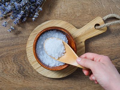 hand scoops out epsom salts with wooden spoon for relaxing bath time