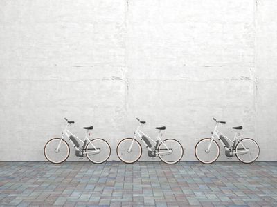 Row of three parked electric bicycles in front of concrete wall