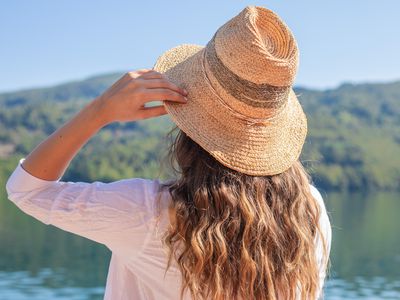 woman wears a big straw hat and stands on edge of lake in hot summertime