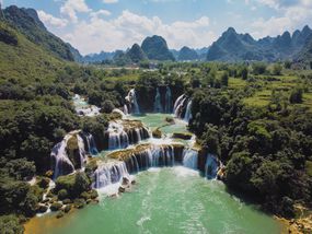 Multi-level Ban Gioc–Detian Falls surrounded by lush, green scenery and falls flowing into clear, green water