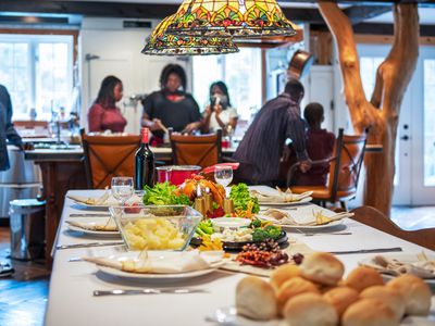 dinner table filled with thanksgiving feast with family mingling in kitchen
