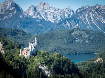 Aerial view of Neuschwanstein Castle surrounded by mountains and lush, green foliage