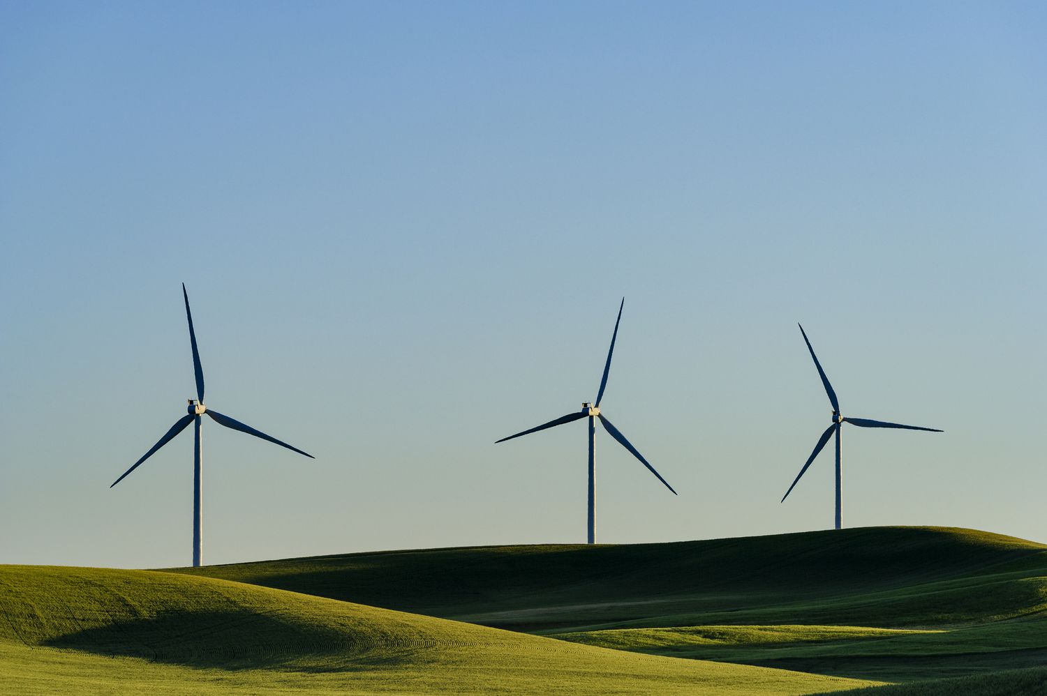 Three wind turbines on a landscape of rolling hills and blue sky.