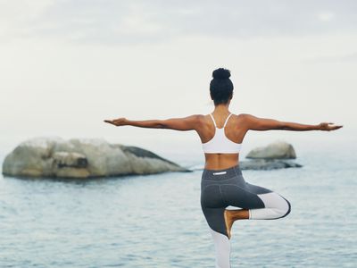 Trusting my balance - stock photo Rearview shot of an unrecognizable woman standing and doing yoga alone by the ocean during an overcast day
