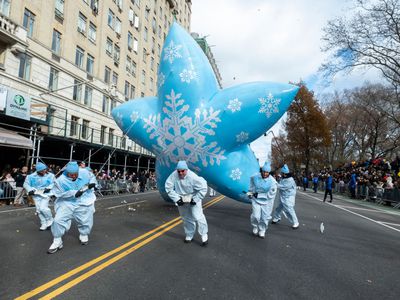 workers in white suits pull large balloon through Macy's Thanksgiving Day Parade