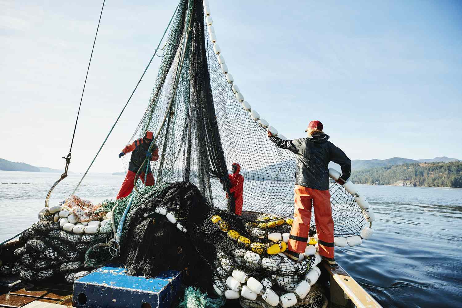 Fishers maneuvering a fishing net on a commercial fishing vessel.