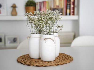 Painted white mason jars with flowers on a table.