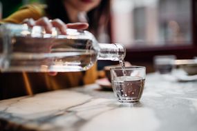A woman pours a glass of water from a glass bottle