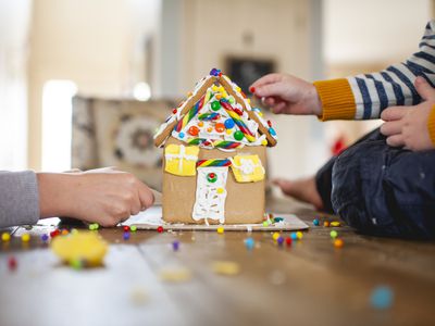 two kids sit on floor and make gingerbread house with candy for christmas