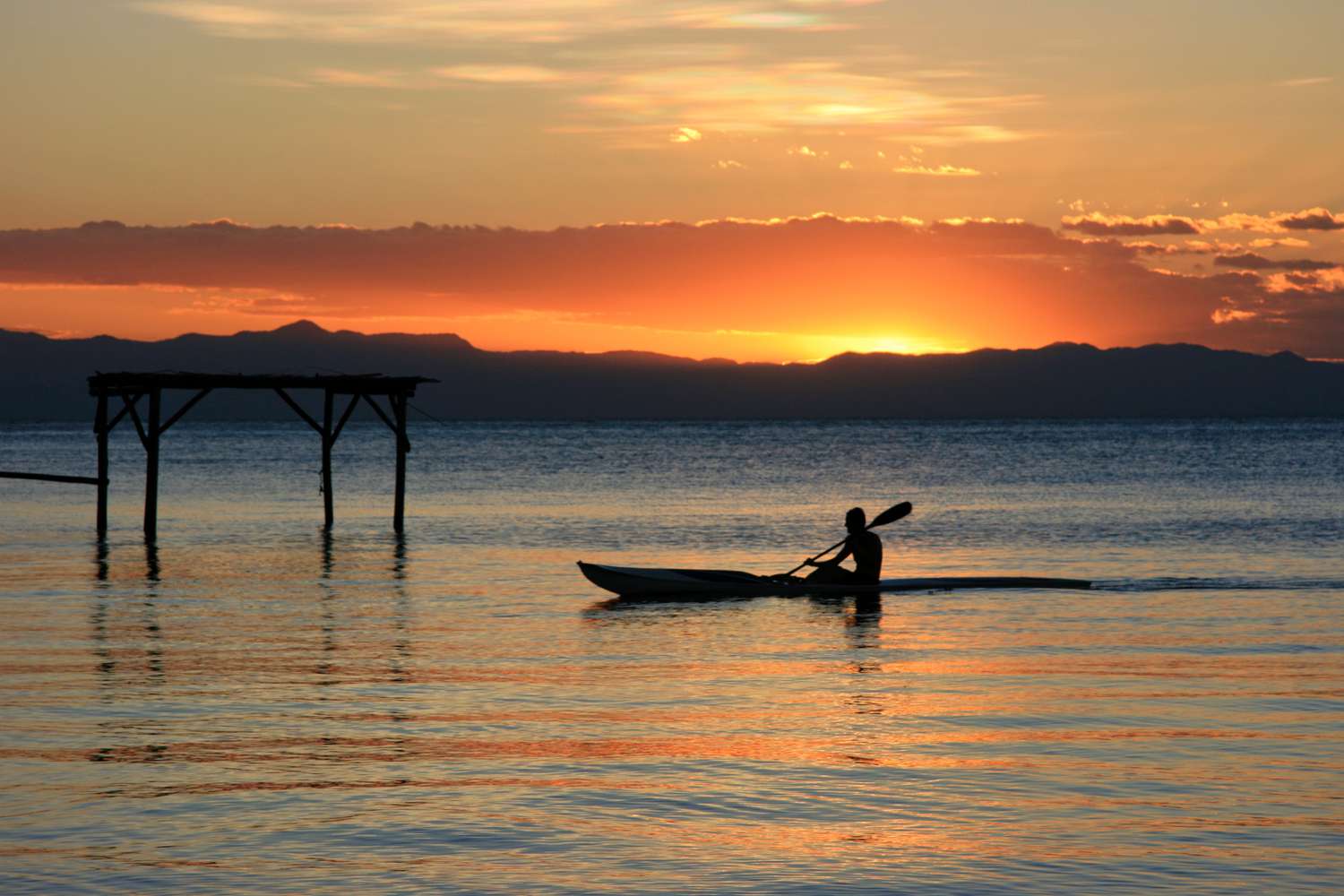 Single kayaker on Lake Malawi with vivid orange and yellow sunset in the distance