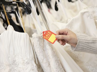Cropped shot of female hands holding price tag attached to wedding gown in bridal boutique