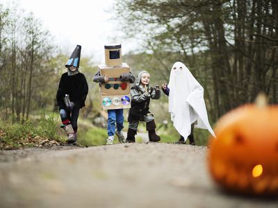 four kids in various Halloween costumes play outside in woods