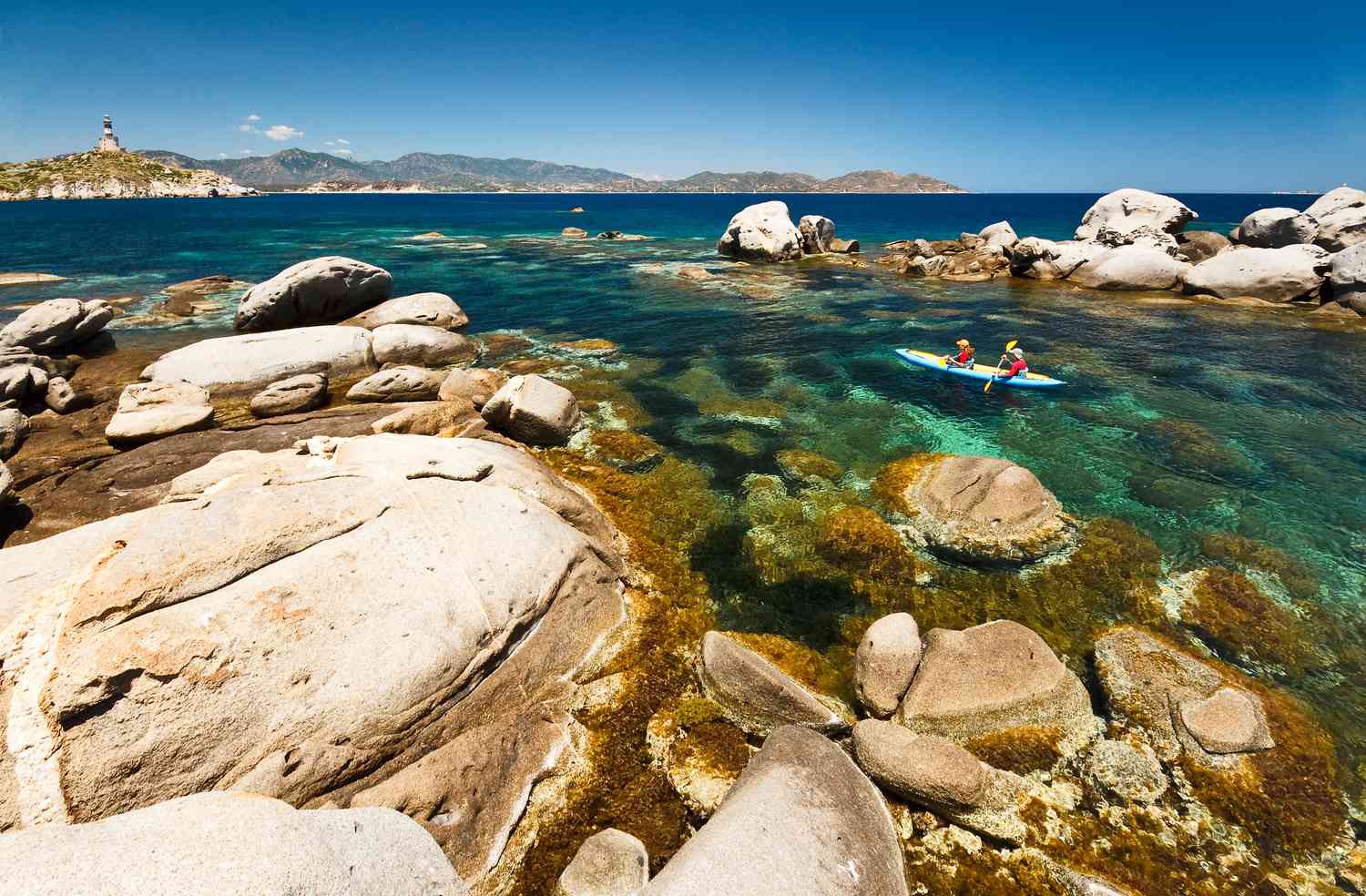 pair of kayakers in the crystal clear waters surrounded by rocks off the southern coast of Sardinia