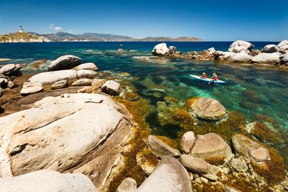 pair of kayakers in the crystal clear waters surrounded by rocks off the southern coast of Sardinia