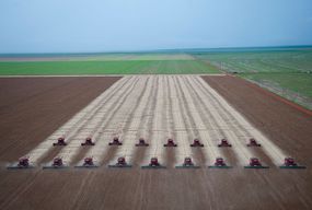 Rows of combines harvest soybeans at a farm in Mato Grosso, Brazil with green fields on the periphery.