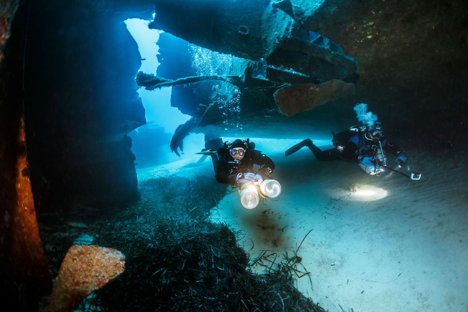 Two scuba divers with bright lights swimming through the wreck Um El Faroud in Malta