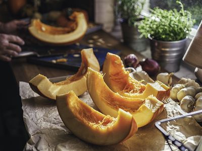 Cutting a fresh pumpkin into slices in a rustic kitchen.