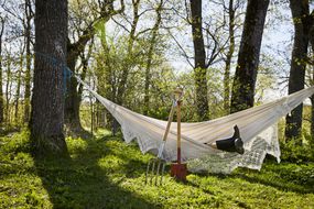 An obscured person in garden boots rests in a hammock with gardening tools resting on the edge