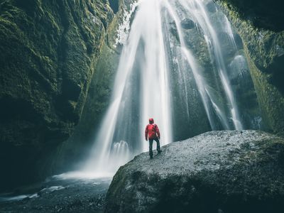 Tourist on a rock admiring Gljufrabui waterfall, Iceland