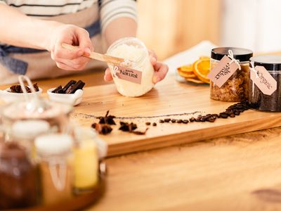 A woman makes homemade body scrubs with organic ingredients on a wood counter.