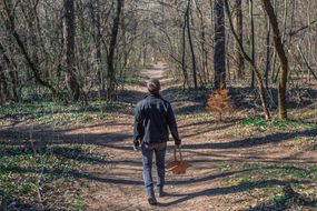 man stands alone in woods at a dirt road crossway with a basket in hand