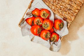 woven basket filled with bright red persimmon fruits and gray linen