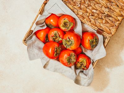 woven basket filled with bright red persimmon fruits and gray linen