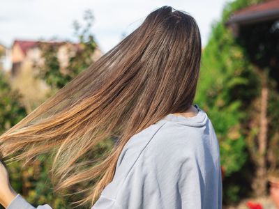 woman in gray t-shirt pulls long shiny hair with her hands while outside