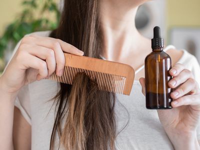 woman holds glass bottle of moringa oil to comb through long hair for moisture