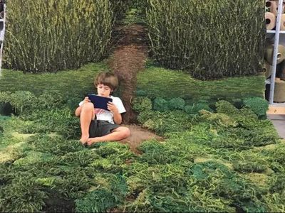 Child reading a book inside on a rug that looks like meadow