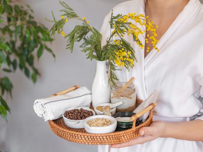 woman in white robe holds tray of natural ingredients for skin softening