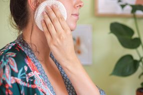 woman cleans face with reusable white cloth pad while wearing silky robe