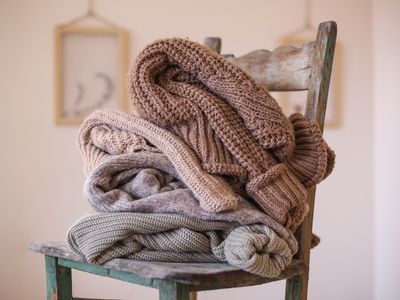 cozy chunky sweaters in earth tones are piled up on wooden chair