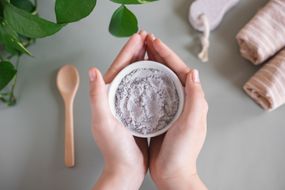 two hands hold gray bentonite clay in bowl for beauty treatments